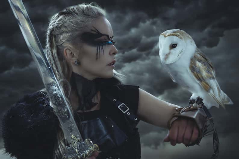 woman wearing face paint holding an owl and a sword