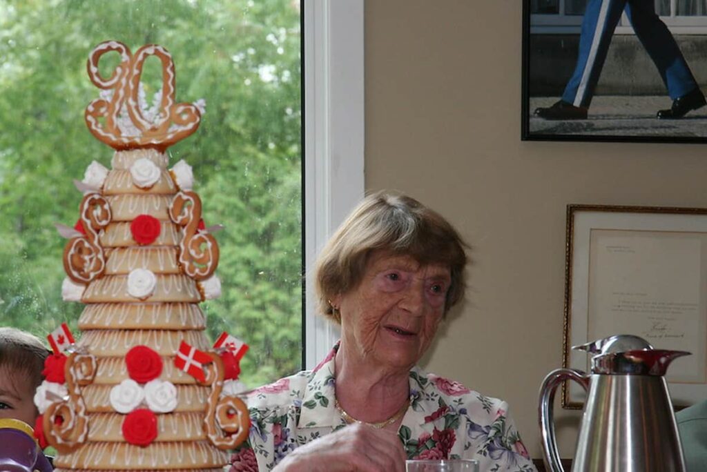 an old woman celebrating her 90th birthday sitting near a cake with danish flags as part of danish birthday traditions