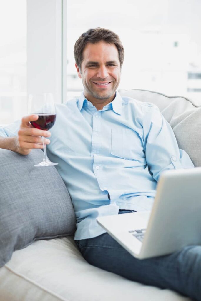 a man holding a glass with wine while watching Scandinavian tv shows on his laptop