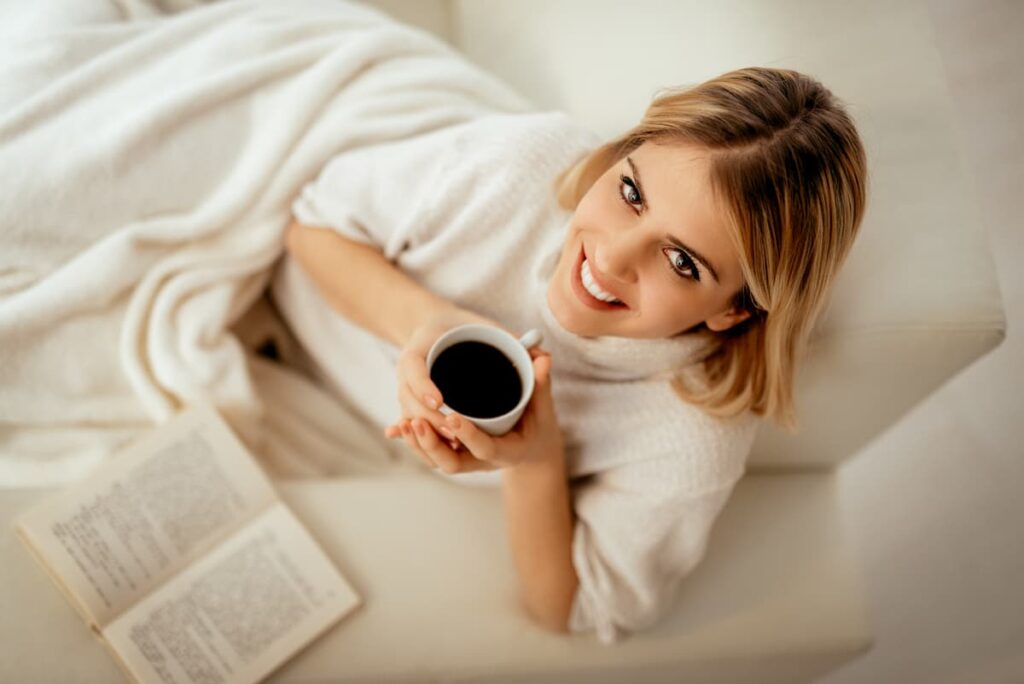 a woman holding a cup of coffee with a book about hygge qoutes